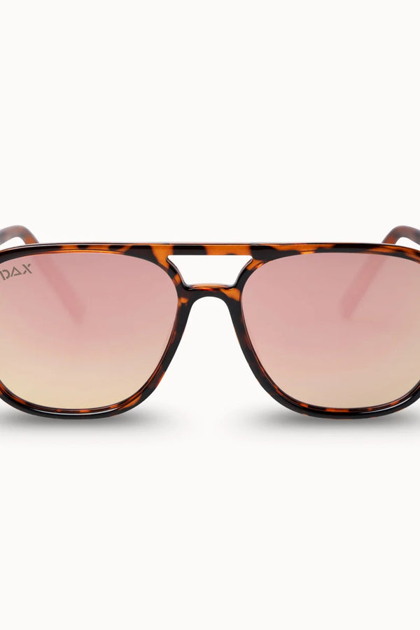 A pair of DAX brand sunglasses with a classic brown and black tortoiseshell frame and pink gradient lenses, shown against a clean off-white background.